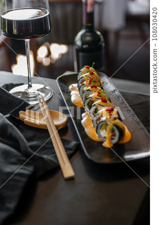 Sushi roll with tuna and vegetables in sauce on a black plate in a restaurant 108030420
