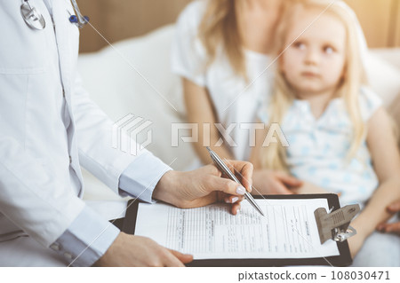 Doctor and patient. Pediatrician using clipboard while examining little girl with her mother at home. Sick and unhappy child at medical exam 108030471
