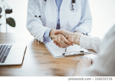Doctor and patient shaking hands above the wooden table in clinic. Medicine concept 108030726