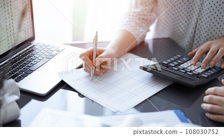 Woman accountant using a calculator and laptop computer while counting taxes for a client. Business audit concepts 108030752