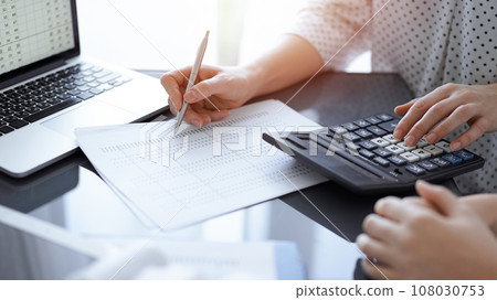 Woman accountant using a calculator and laptop computer while counting taxes for a client. Business audit concepts 108030753