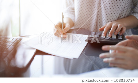 Woman accountant using a calculator and laptop computer while counting and discussing taxes with a client. Business audit concepts 108030754