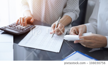 Woman accountant using a calculator and laptop computer while counting taxes with a client or colleague. Business audit team Woman accountant using a calculator and laptop computer while counting taxes with a client or colleague. Business audit team 108030756