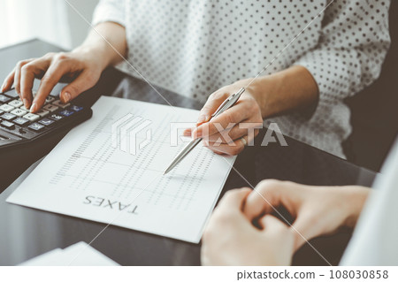 Woman accountant using a calculator and laptop computer while counting taxes for a client. Business audit and finance concepts Woman accountant using a calculator and laptop computer while counting taxes for a client. Business audit and finance concepts 108030858