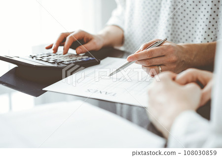 Woman accountant using a calculator and laptop computer while counting taxes for a client. Business audit and finance concepts Woman accountant using a calculator and laptop computer while counting taxes for a client. Business audit and finance concepts 108030859