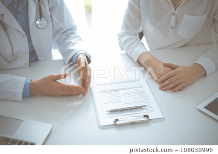 Doctor and patient discussing current health questions while sitting near of each other and using clipboard at the table in clinic, just hands closeup. Medicine concept Doctor and patient discussing current health questions while sitting near of each other and using clipboard at the table in clinic, just hands closeup. Medicine concept 108030996