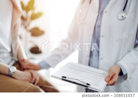 Doctor and patient discussing health exam results. Friendly physician reassuring a young woman by one hand while keeping clipboard with medical papers in another. Medicine concept 108031037