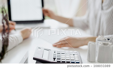 Calculator is lying at the white table near two female accounters counting taxes or making revenue balance. Business audit and finance concepts 108031089