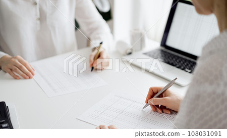 Two accountants using a laptop computer for counting taxes at white desk in office. Teamwork in business audit and finance Two accountants using a laptop computer for counting taxes at white desk in office. Teamwork in business audit and finance 108031091