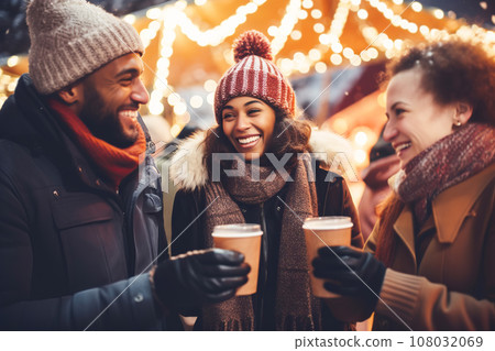 Multiracial friends drinking mulled wine at Christmas fair in festively decorated city 108032069
