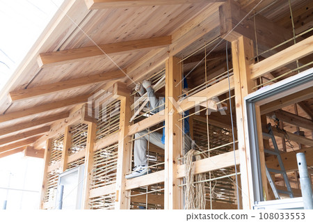 A craftsman is plastering the base of a mud wall at a construction site for a wooden house. 108033553