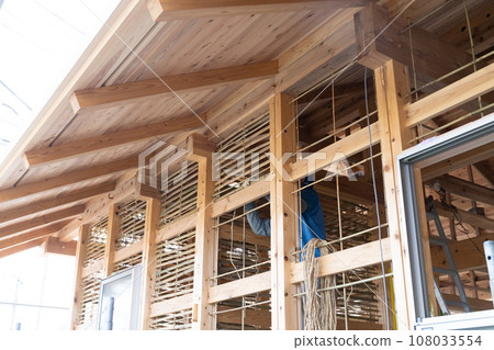 A craftsman is plastering the base of a mud wall at a construction site for a wooden house. A craftsman is plastering the base of a mud wall at a construction site for a wooden house. 108033554