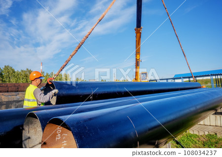 Slinger unloads large gasification pipes on summer day. Pipes for transporting natural gas Slinger unloads large gasification pipes on summer day. Pipes for transporting natural gas 108034237