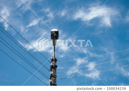 View of street lamp on concrete pole with wires against blue sky on summer day. View from bottom to 108034239