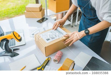 startup young female small business owners attaching shipping labels to cardboard boxes or parcels for delivery of customer orders-concept shopping online startup young female small business owners attaching shipping labels to cardboard boxes or parcels for delivery of customer orders-concept shopping online 108035366