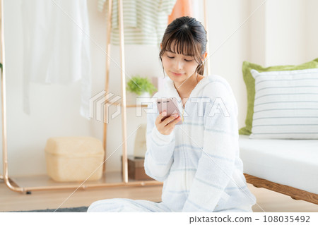 Young woman looking at her smartphone in the living room Young woman looking at her smartphone in the living room 108035492