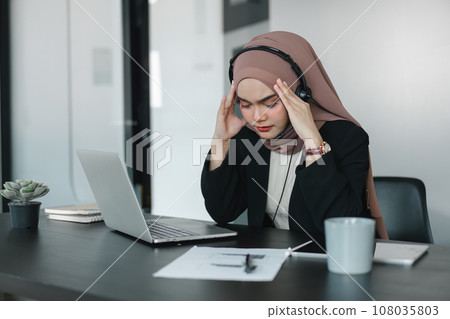 Asian muslim operator woman agent with headsets working in a call centre. Asian muslim operator woman agent with headsets working in a call centre. 108035803