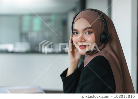 Asian muslim operator woman agent with headsets working in a call centre. Asian muslim operator woman agent with headsets working in a call centre. 108035810