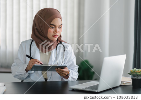 Young muslim female doctor in brown hijab headscarf working with medical papers while sitting in modern clinic office. 108035818