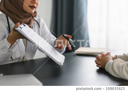 Young muslim female doctor in brown hijab headscarf having appointment consulting female patient in modern clinic hospital. Medical healthcare concept. 108035825