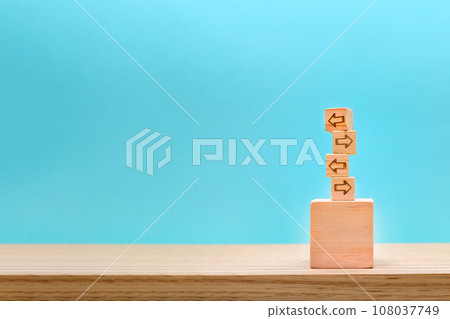 A wooden cube sign with arrows pointing in alternating directions on a blue background on a desk 108037749