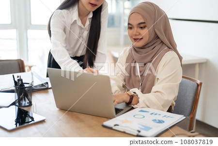 An attractive Asian businesswoman and a beautiful Asian-Muslim businesswoman are working together. 108037819