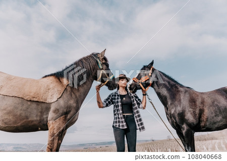 Young happy woman in hat with her horse in evening sunset light. Outdoor photography with fashion model girl. Lifestyle mood. Concept of outdoor riding, sports and recreation. Young happy woman in hat with her horse in evening sunset light. Outdoor photography with fashion model girl. Lifestyle mood. Concept of outdoor riding, sports and recreation. 108040668