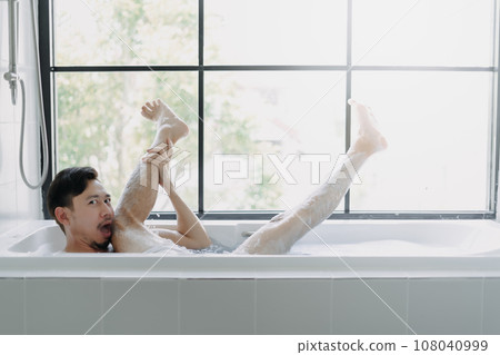 Funny man lying in the bathtub showing his leg pretend to be a sexy woman. 108040999