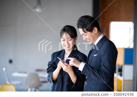Male and female speaking while watching a smartphone 108042436