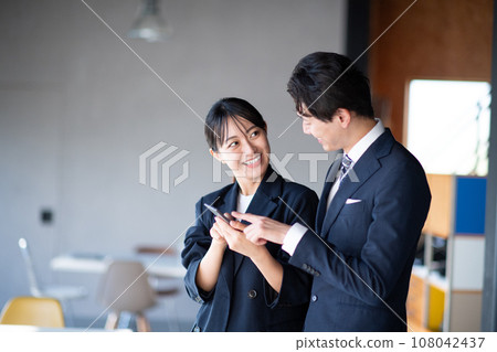 Male and female speaking while watching a smartphone 108042437