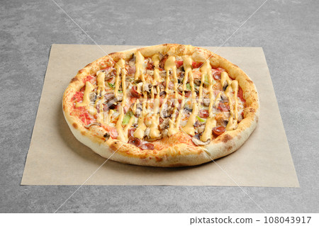 Pizza with thin sausage and champignon on parchment paper Pizza with thin sausage and champignon on parchment paper 108043917