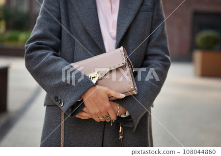 Close up of female hands holding fashion accessory beige leather handbag. Detail of stylish outfit Close up of female hands holding fashion accessory beige leather handbag. Detail of stylish outfit 108044860