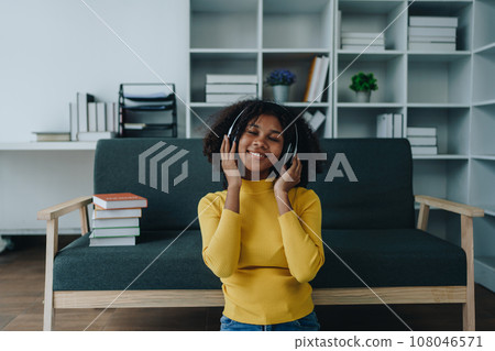 Happy young African American latina woman listening to music using headphones at home living room. relaxing, relax, relaxation concepts. Happy young African American latina woman listening to music using headphones at home living room. relaxing, relax, relaxation concepts. 108046571