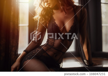 Low section of woman posing in black lingerie and sexy nylons, with an emphasis on her silhouette against a bright window. Creating a sensual and seductive aesthetic. Generative Ai 108047231