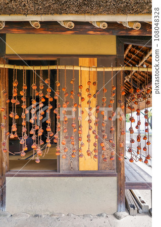 Autumn dried persimmons hanging under the eaves of a farmhouse 108048328