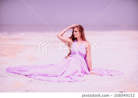 Pink lake woman. A woman in a pink dress sits on the salty shore of a pink lake and poses for a souvenir photo, creating lasting memories. Pink lake woman. A woman in a pink dress sits on the salty shore of a pink lake and poses for a souvenir photo, creating lasting memories. 108049152