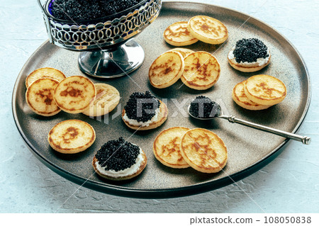 Blinis with black caviar and cream cheese, on a festive dish, mini pancakes 108050838