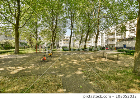 an empty park with trees in the fore, and buildings in the background on a bright sunny day stock photo 108052032