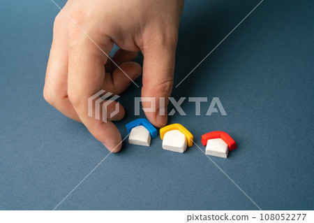 Choose from housing options. The hand picks up one of the house figures. Guidance and help to navigate the different mortgage options. Comparing interest rates and fees. Choose from housing options. The hand picks up one of the house figures. Guidance and help to navigate the different mortgage options. Comparing interest rates and fees. 108052277