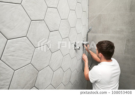 Man plumber installing handheld showerhead in bathroom. Male worker fixing metal bath showerhead and doing plumbing works while working on home renovation. 108053408