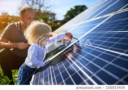 Man showing his small child the solar panels during sunny day. Father presenting to son modern energy resource. Little steps to alternative energy. Man showing his small child the solar panels during sunny day. Father presenting to son modern energy resource. Little steps to alternative energy. 108053409