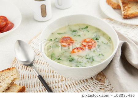 Typical Portuguese soup Caldo Verde with bread and chorizo sausage on gray background 108053486