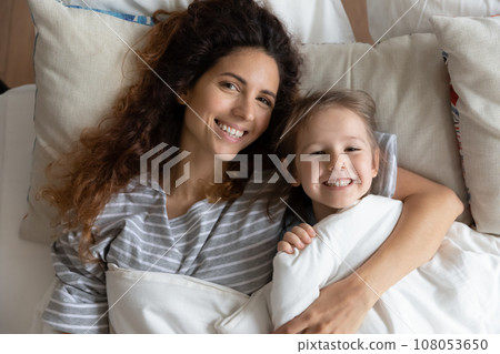 Portrait of happy mom and little daughter cuddle in bed Portrait of happy mom and little daughter cuddle in bed 108053650