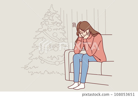 Woman is sitting on sofa near christmas tree and is sad because of loneliness and lack of friends 108053651