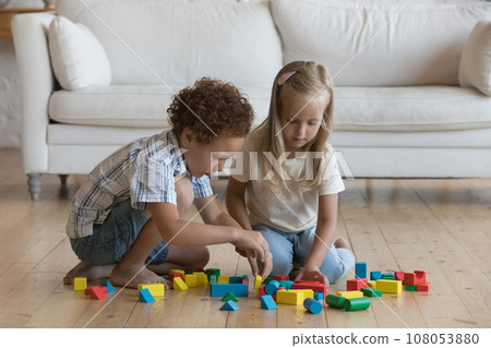 Two focused little kids playing on floor at home Two focused little kids playing on floor at home 108053880