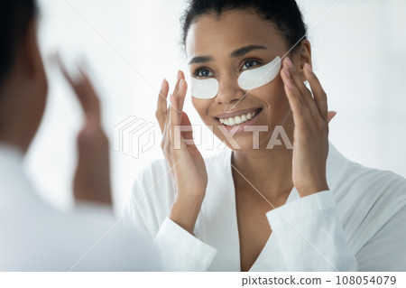 Biracial young woman apply under eye patches in bath 108054079