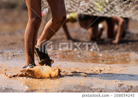 Mud race runners. Crawling, passing under a net obstacle during extreme obstacle race Mud race runners. Crawling, passing under a net obstacle during extreme obstacle race 108054245