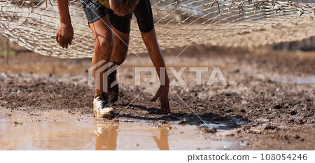 Mud race runners. Crawling, passing under a net obstacle during extreme obstacle race Mud race runners. Crawling, passing under a net obstacle during extreme obstacle race 108054246