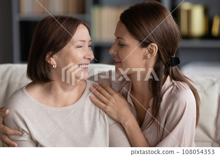 Adult daughter hugs lovely aged mother seated on couch 108054353
