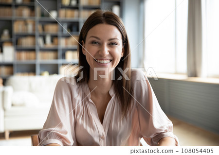 Happy millennial woman sitting indoors laughing looking at camera 108054405